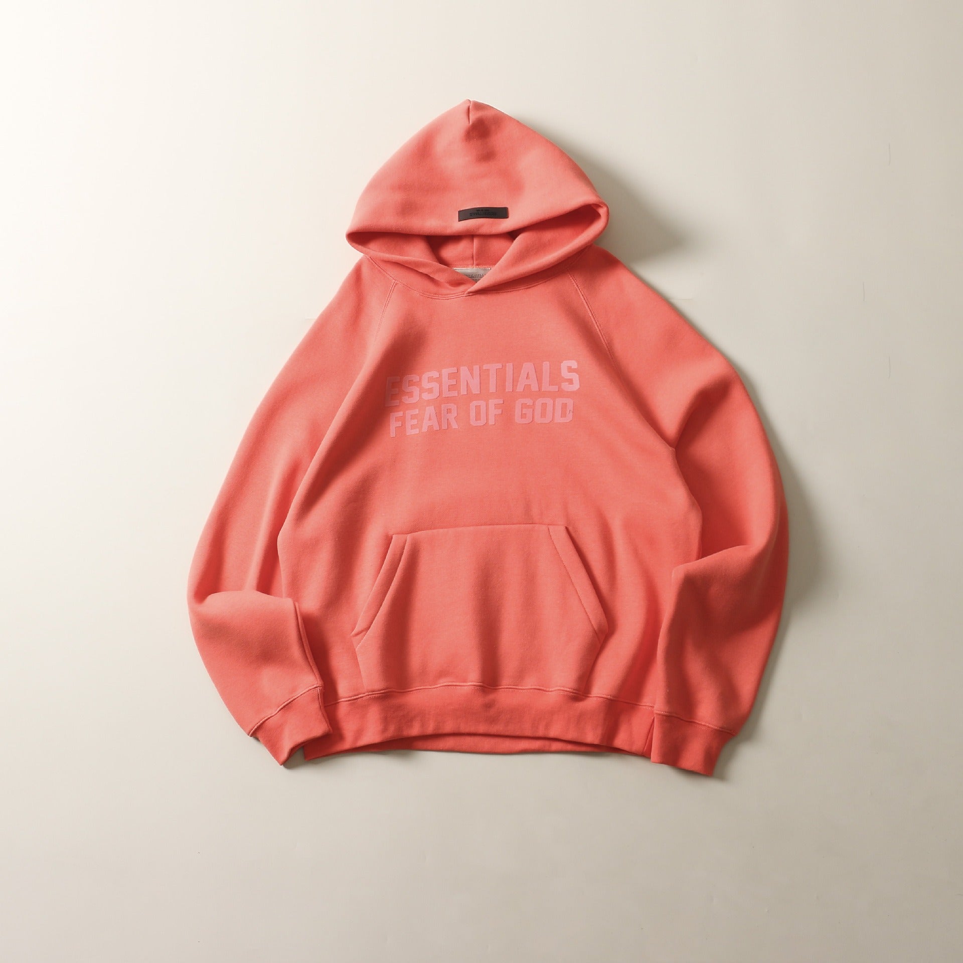 Vibrant coral-colored hoodie with printed text design, showcasing a modern, trendy streetwear style.