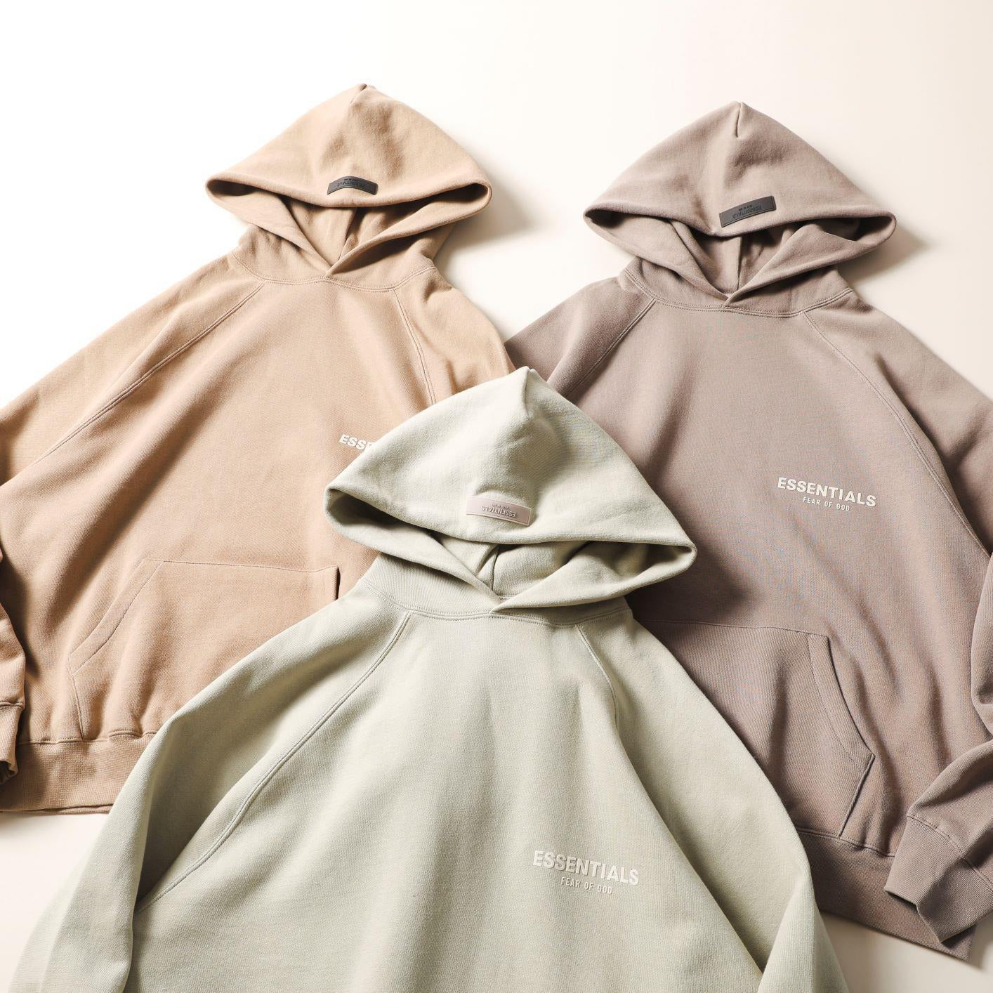 Oversized hooded sweatshirts with "ESSENTIALS" printed on the chest in a loose, trendy street style. The hoodies come in a variety of neutral, earthy tones, creating a cohesive and stylish collection.