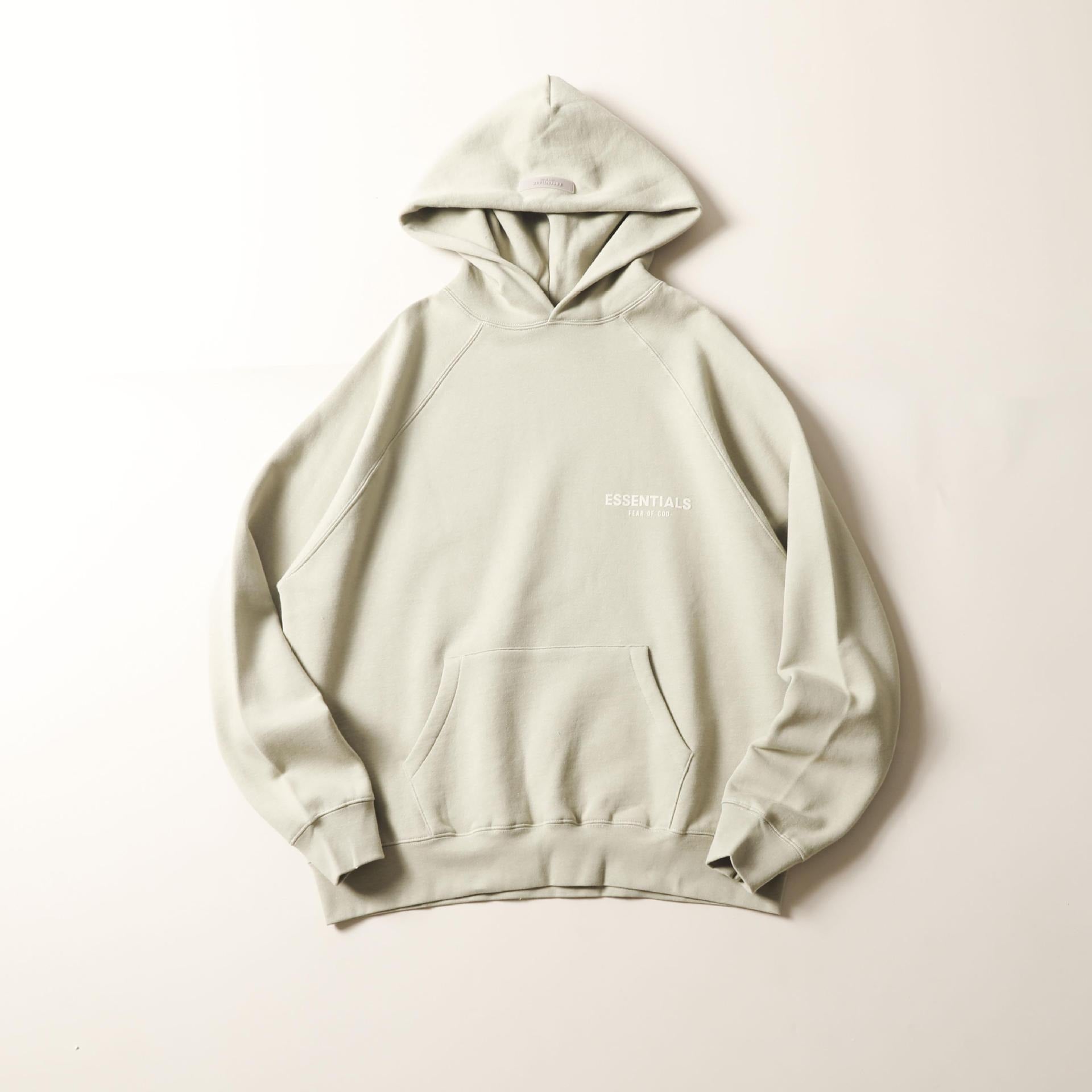 Oversized light gray hooded sweatshirt with a large chest pocket and front logo print, displayed on a plain background